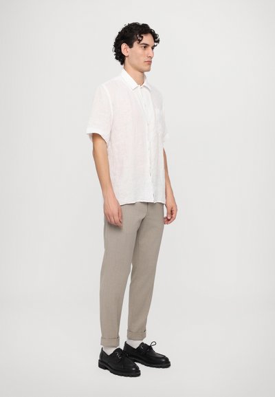 Camisa de lino blanca de manga corta, pantalones ajustados gris claro y zapatos negros con suela gruesa, con puños enrollados y un solo bolsillo en el pecho.