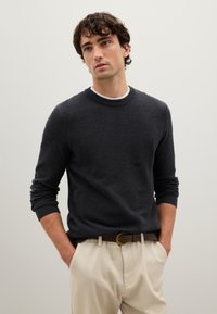 Pullover grigio scuro lavorato a maglia con scollo rotondo e polsini a coste, abbinato a pantaloni beige e una cintura marrone. Design semplice e testurizzato.