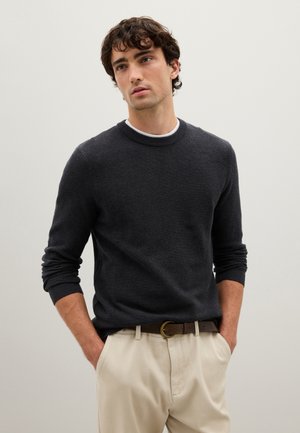 Pull en tricot gris foncé avec un col rond et des poignets côtelés, associé à un pantalon beige et une ceinture marron. Design texturé simple.