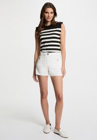 Top senza maniche a righe bianche e nere con dettagli sulle spalle, abbinato a shorts in denim bianco a vita alta con tasche frontali e bottone.
