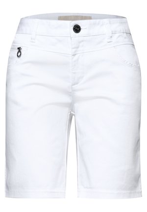 Close-up af en person iført hvide bukser med en lynlåslomme med en sølv ring træk, og en rød top, der er delvist synlig.