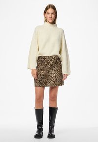 Kremfarget strikket turtleneck-genser kombinert med en leopardmønstret mini-skjørt. Modellen har på seg knelengde svarte lærstøvler.