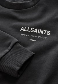 Černá mikina s žebrovanými lemy na rukávech s bílým nápisem "ALLSAINTS", japonskými znaky a nápisem "LONDON" na hrudi.