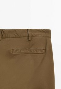 Gros plan sur la partie supérieure arrière d'un pantalon marron montrant une passante de ceinture et une poche passepoilée unique sur fond blanc.