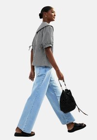 Svartvitt rutigt skjorta med puffärmar och stor krage, kombinerad med ljusblå vida jeans och en strukturerad svart bucket bag.