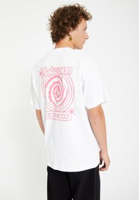 White cotton t-shirt featuring a pink spiral design and "Volcom Stone Co." text on the back, round neck, and short sleeves.