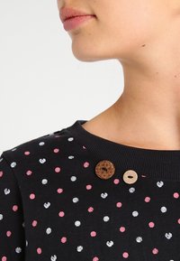 Sudadera negra con lunares multicolores en rosa y plata. Presenta dos botones decorativos: uno de madera y otro de color claro.