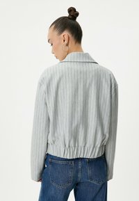 Chaqueta gris a rayas con cuello, dobladillo elástico y ajuste relajado, combinada con unos vaqueros de denim azules. Textura suave.