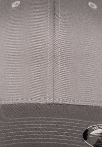 Cappellino da baseball grigio realizzato in tessuto testurizzato con visiera curva. Presenta accenti cuciti e un logo su un'etichetta sul davanti.