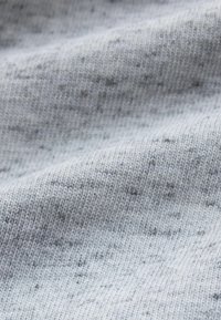 Lichtgrijze gebreide stof met een zachte textuur, voorzien van subtiele donkerdere vlekjes overal en een fijn, gelijkmatig weefpatroon.