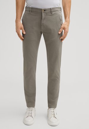 Helle graue Baumwollhose mit schmalem Schnitt, mit Knopfverschluss und Seitentaschen, kombiniert mit weißen Sneakers.