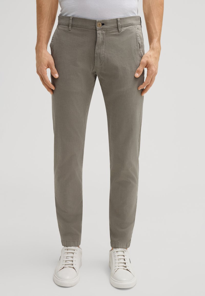 Pantaloni in cotone grigio chiaro con vestibilità affusolata, dotati di chiusura a bottone e tasche laterali, abbinati a sneaker bianche.