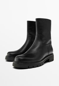 Černé kožené kotníkové boty s hladkým povrchem, kulatou špičkou a robustní protiskluzovou podrážkou. Minimalistický design, bez viditelného kovového prvku nebo akcentu.