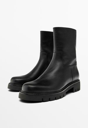 Stivali alla caviglia in pelle nera con una texture liscia, punta rotonda e suola spessa con battistrada. Design minimalista, senza hardware o accenti visibili.