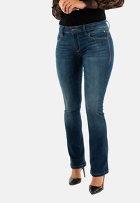 Vaqueros de denim azul de pierna recta con costuras en contraste, bolsillos frontales y cremallera. Llevados con tacones altos negros.