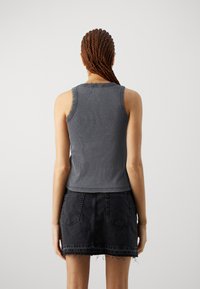 Hallide hallitusseente top, millel on ribad ja must denim mini seelik, millel on kulunud äär ja tagataskud; nähtud selja tagant.
