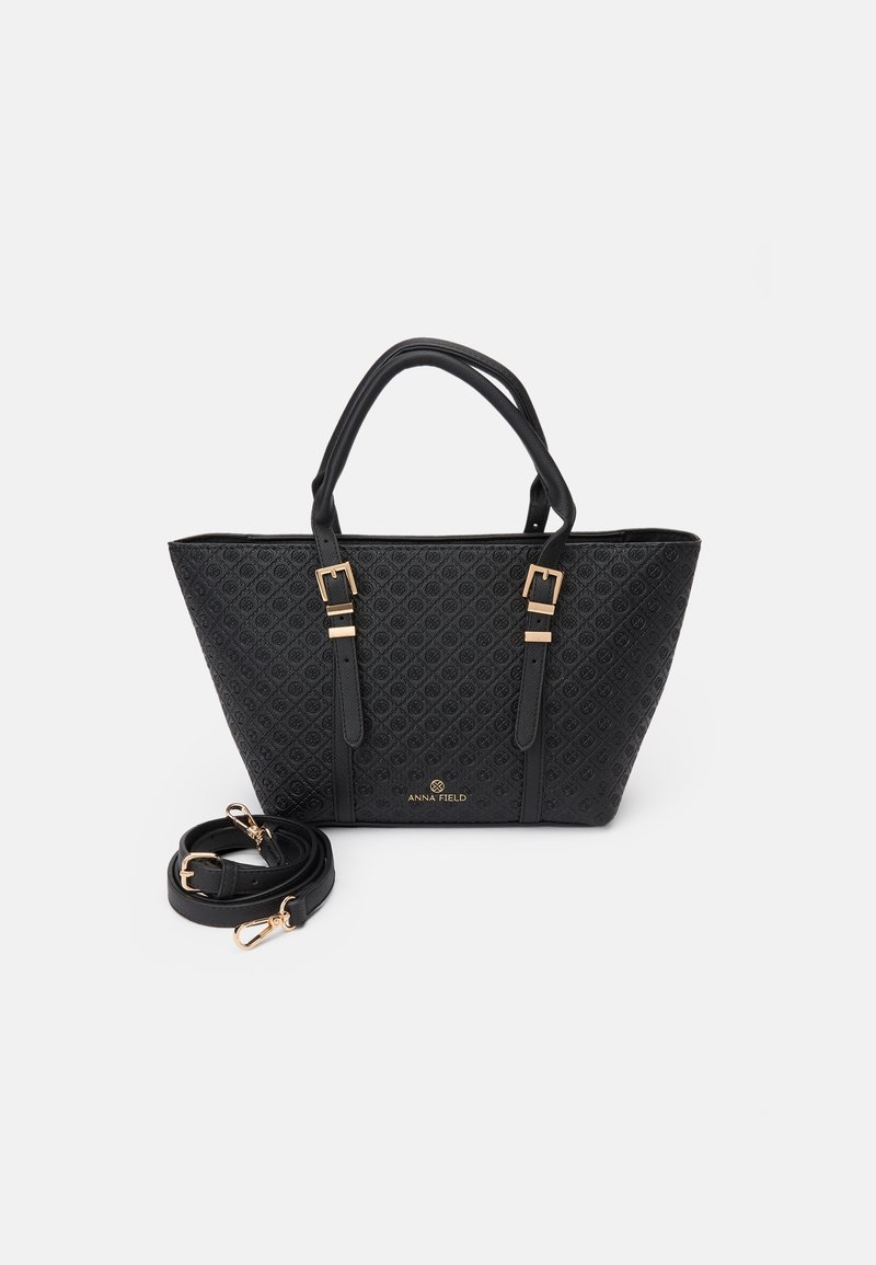 Sac à main noir avec un motif texturé subtil, des boucles dorées, deux poignées et une bandoulière amovible placée devant.