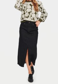 Schwarzer Jeansrock mit einem vorderen Schlitz und fransigem Saum, kombiniert mit einem gemusterten Langarmpullover, der florale Designs in hellen und dunklen Tönen zeigt.