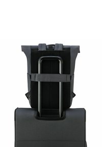 Mochila de tela negra con respaldo acolchado, correas ajustables y un diseño de malla, sujeta de manera segura al mango de una elegante maleta negra.