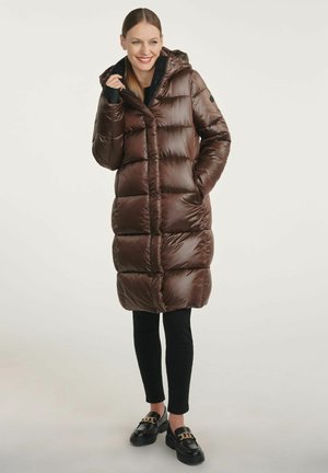 Brązowa kurtka puchowa z kapturem, posiadająca pikowane sekcje, zamek błyskawiczny z przodu i kieszenie po bokach, zestawiona z czarnymi spodniami i butami.