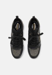 Schwarze Sportschuhe mit einem gestrickten Obermaterial und einem strukturierten, gemusterten Stoff. Mit goldenen Akzenten, runden Schnürsenkeln und einem gepolsterten Kragen.