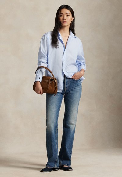 Cămașă albastru deschis cu nasturi și mâneci lungi, blugi evazați de culoare albastru închis, geantă maro și pantofi negri cu cusături albe.