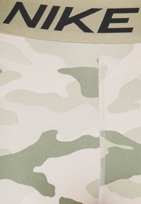 Slip con cintura in pelle d'oca a motivo camouflage Nike, caratterizzati da una texture liscia in tonalità beige chiaro e verde con un logo nero a contrasto.