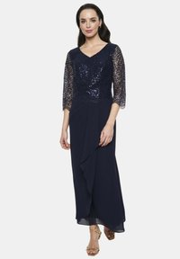 Nawigoniebna sukienka w kolorze granatowym z koronkowym topem pokrytym cekinami oraz rękawami do trzech czwarte. Spódnica w swobodnym stylu z bocznym detalem drapowanym i warstwowym materiałem.