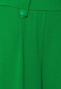 Pantalon vert avec un tissu lisse et texturé, doté d'un unique bouton assorti à la taille et d'un design à plissé à l'avant.