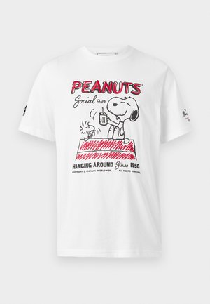 Fehér póló piros és fekete Peanuts grafikával, amelyen Snoopy és Woodstock láthatóak egy kutyaházon, amint italt tartanak a kezükben, a szöveg "Peanuts Social Club" mellett.