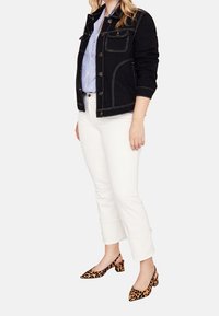 Schwarze Jeansjacke mit weißen Nähten, kombiniert mit einem hellblauen gestreiften Hemd, weißen Capri-Hosen und Slingback-Absätzen im Leopardenmuster.