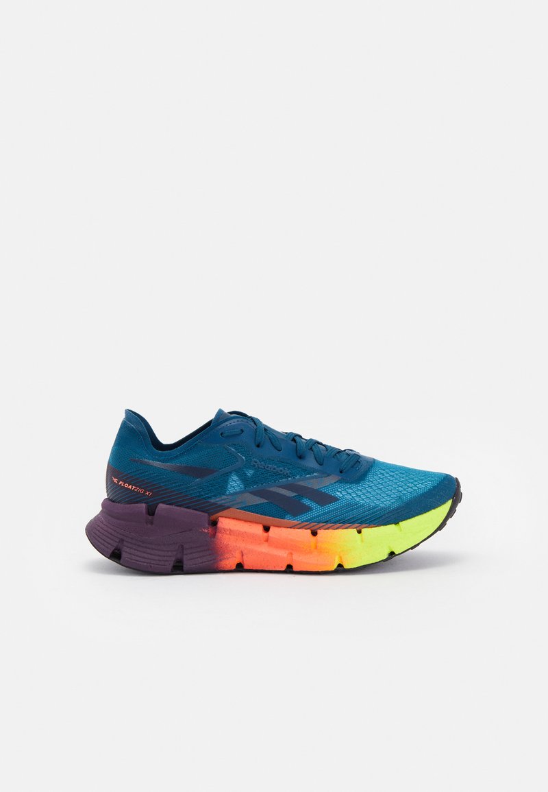 Zapatilla deportiva azul con parte superior de malla texturizada, media suela en degradado púrpura y neón, y suela exterior de goma negra. Cierres y logotipo en colores contrastantes.