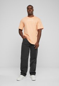T-shirt rayée orange avec des lignes blanches et un logo, associée à un pantalon gris foncé et des baskets blanches. Coupe décontractée avec un design relax.