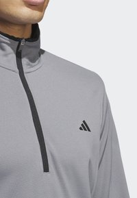 Veste zippée grise avec un col montant, dotée d'une fermeture éclair noire et d'accents noirs. Comprend un petit logo noir sur la poitrine.