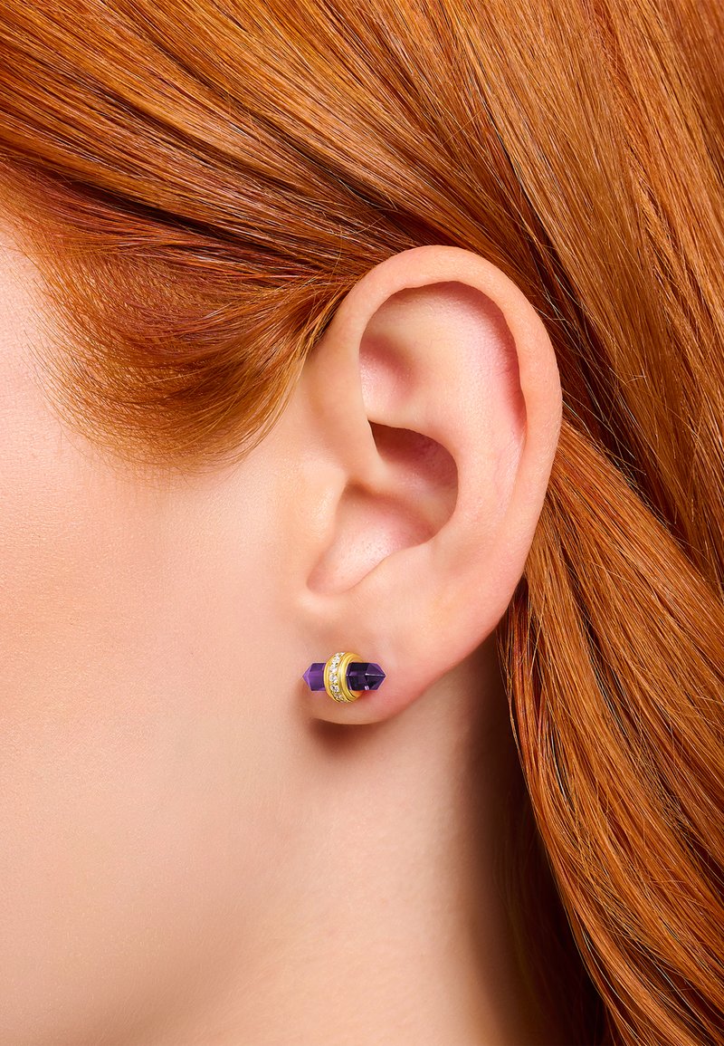 Nahaufnahme von rotem Haar und Ohr, das einen goldenen und lila Edelsteinstud mit kleinen klaren Kristallen trägt.