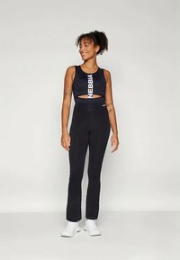 Top sport negru scurt cu detalii decupate și logo-ul "NEBBIA", asortat cu colanți negri cu talie înaltă, purtat cu încălțăminte albă.