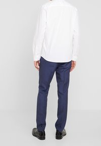 Valkoinen pitkähihaisa paita nappidetaililla, yhdistetty tummansinisiin slim fit -housuihin ja mustiin kenkiin. Ilme on siisti ja virallinen.