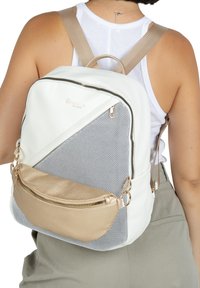 White and gray backpack with a textured surface, a gold zippered pocket, and beige straps; features a geometric design and a mesh panel.