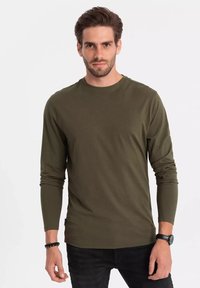 Böjtð er græn long-sleeve skyrta úr mjúku bómull með ljósbrúnan háls og sérsmíðaða hönnun, berst með svörtum gallabuxum og svörtu úrið.