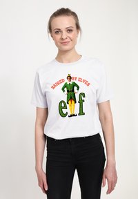 Bílé bavlněné tričko s grafickým motivem a nápisem "RAISED BY ELVES" nad postavičkou skřítka; dominují zelené a žluté barvy.