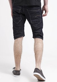 Shorts de mezclilla azul oscuro con un diseño ajustado, que cuentan con dos bolsillos traseros, detalles de costura sutiles y un dobladillo ligeramente desgastado.
