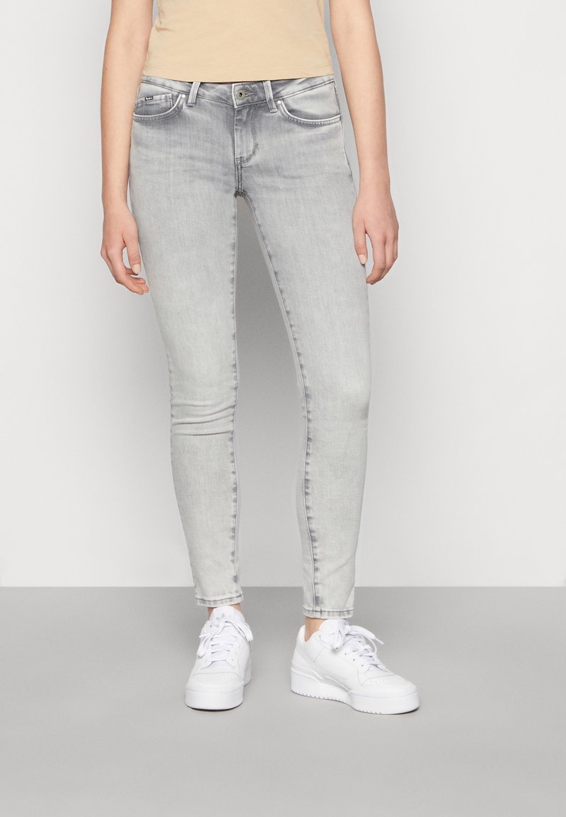 Jeans skinny de color gris claro con un diseño clásico de cinco bolsillos, textura desgastada y acentos cosidos, combinados con zapatillas blancas.