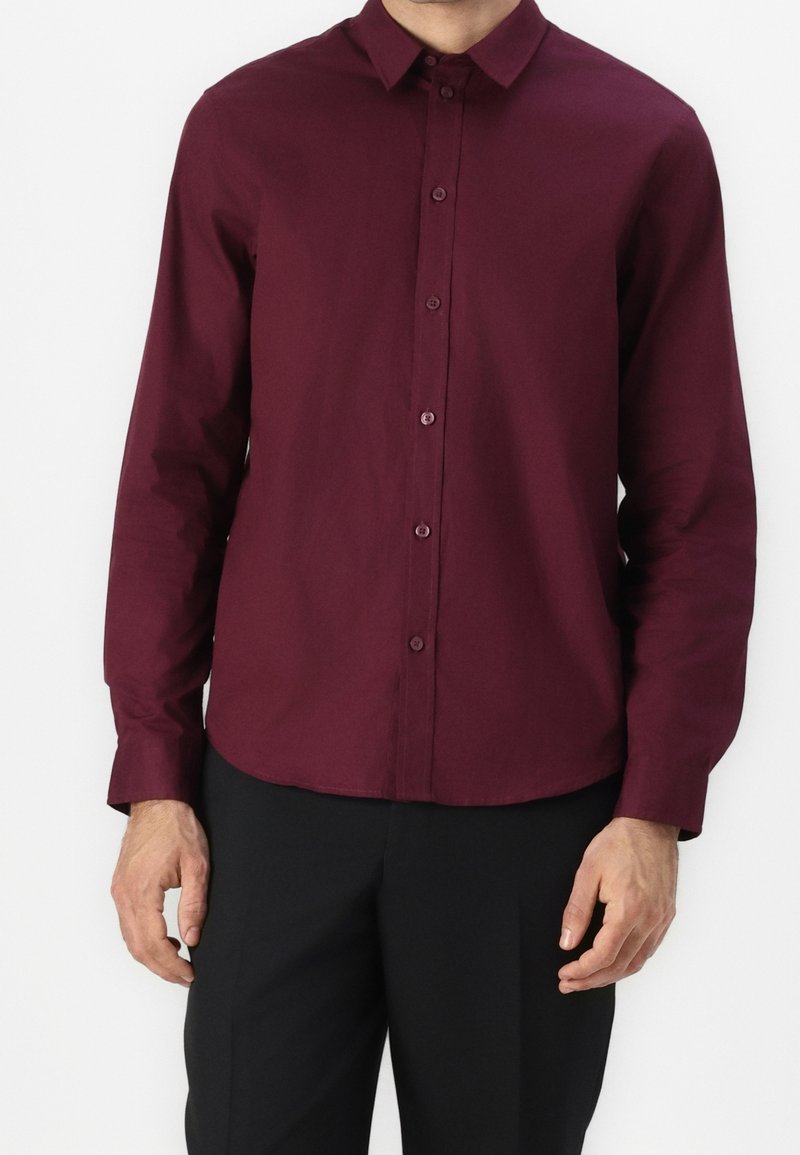 Burgundowa koszula z długim rękawem, klasycznym kołnierzykiem i prostym wykończeniem. Wykonana z gładkiego materiału o subtelnej fakturze.