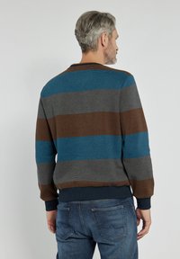 Sweter w paski w niebieskie, brązowe, szare i granatowe poziome linie, z prążkowanymi mankietami i okrągłym dekoltem, w zestawieniu z ciemnymi dżinsami.