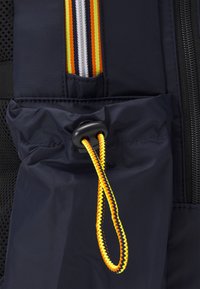Giacca in nylon blu navy con zip e strisce arancioni e gialle. Include una tasca arricciata con stringa intrecciata e fermaglio nero.