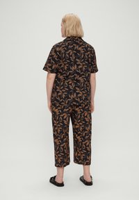 Conjunto de tela negra con un patrón de hojas en tonos tierra, camisa de manga corta y pantalones recortados, diseñado para la comodidad.