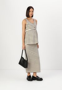 Rochie maxi cu dungi în nuanțe de bej și negru, cu decolteu rotund, talie strânsă, nasturi și asociată cu mocasini negri cu talpă groasă și o poșetă neagră.