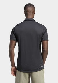 Schwarzes Poloshirt mit kurzen Ärmeln aus glattem Stoff, mit einem Kragen und gesticktem Logostich auf der Schulter, von hinten betrachtet.