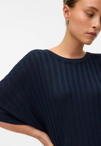 Granatowy sweter z prążkowanego dzianiny, o szerokich rękawach i okrągłym dekolcie, charakteryzujący się miękką fakturą i delikatnym pionowym wzorem.
