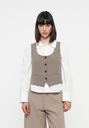 Grijze vest met een ronde halslijn, vijf knopen en zijzakken, gedragen over een witte blouse met kraag en gecombineerd met beige pantalons.
